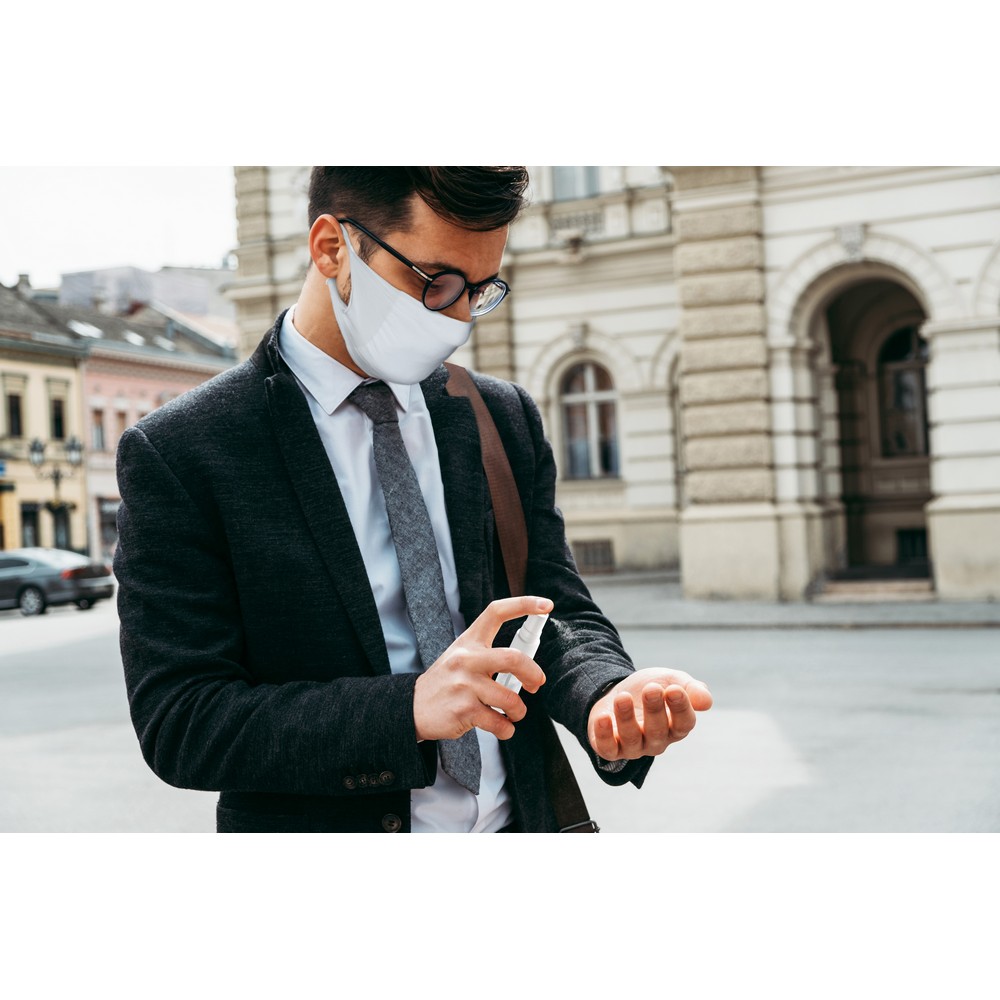 Elegant business man with protective face mask using alcohol spr